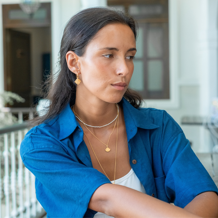 A woman with brown hair in a blue blouse sleeves and a white top together with golden jewellery