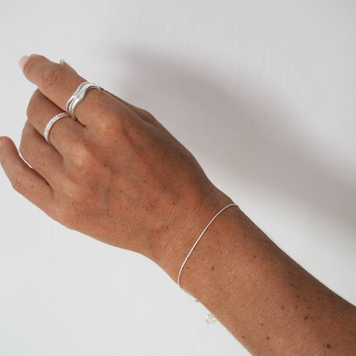 Close-up of a woman's hand wearing silver rings and a delicate silver bracelet.