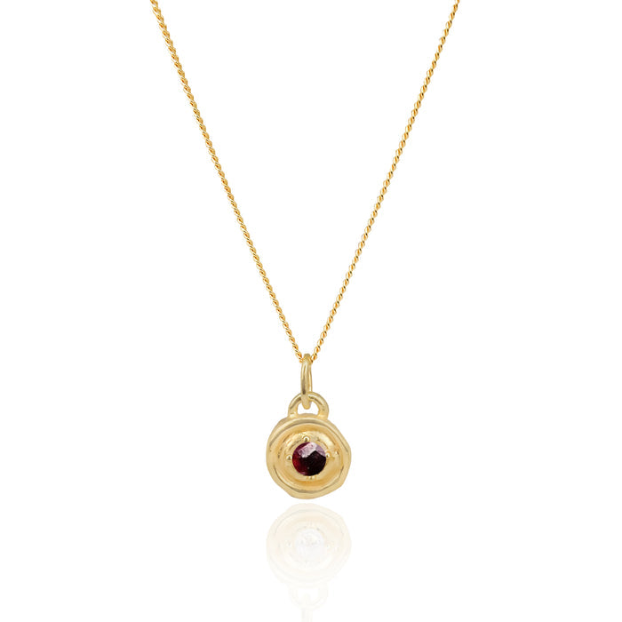 Gold necklace with a round pendant featuring a red gemstone on a white background