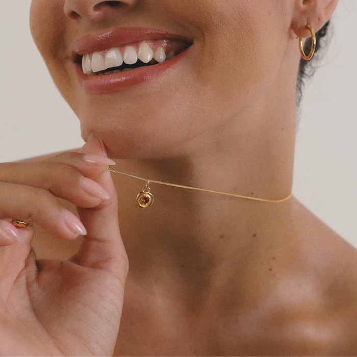 Close-up of a woman wearing a gold necklace with a small round pendant.