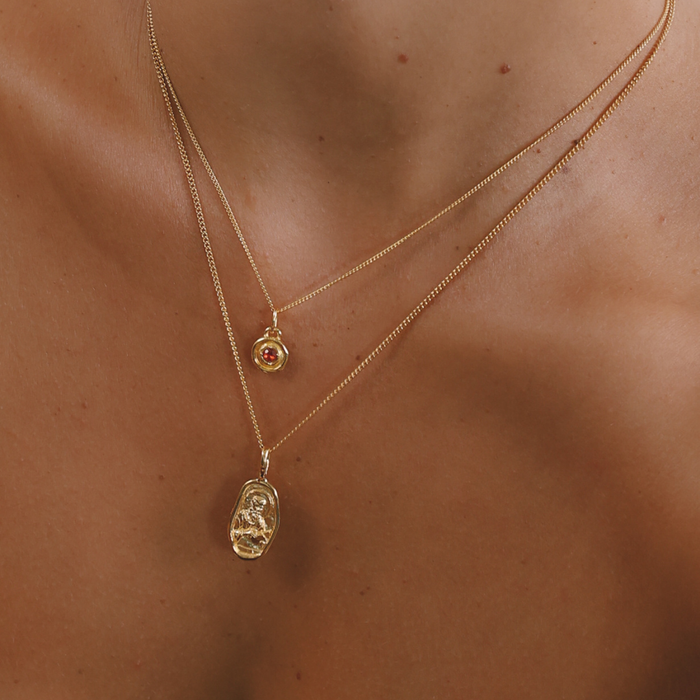 Two gold necklaces with pendants on a person's neck against a neutral background