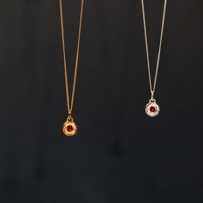 Two gold necklaces with red gemstones on a black background