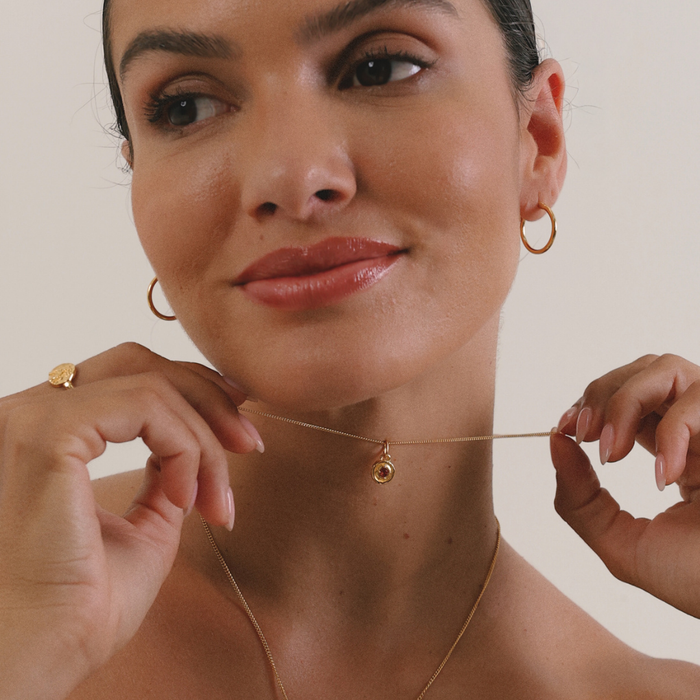 Woman wearing a gold necklace with a small pendant, holding it up to her neck.