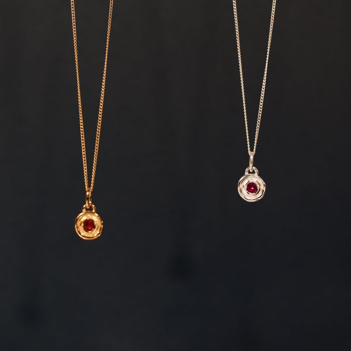 Two gold necklaces with red gemstones on a black background