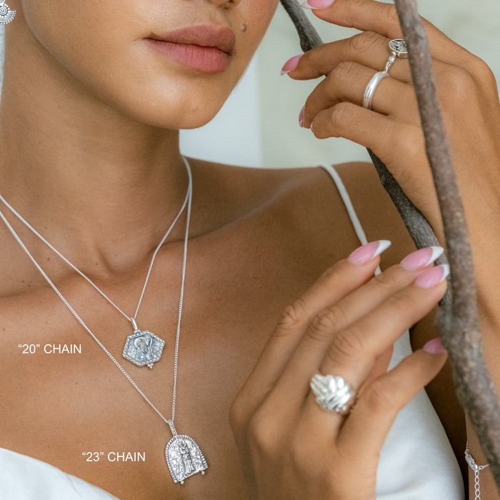 Woman wearing silver necklaces and rings with a neutral background
