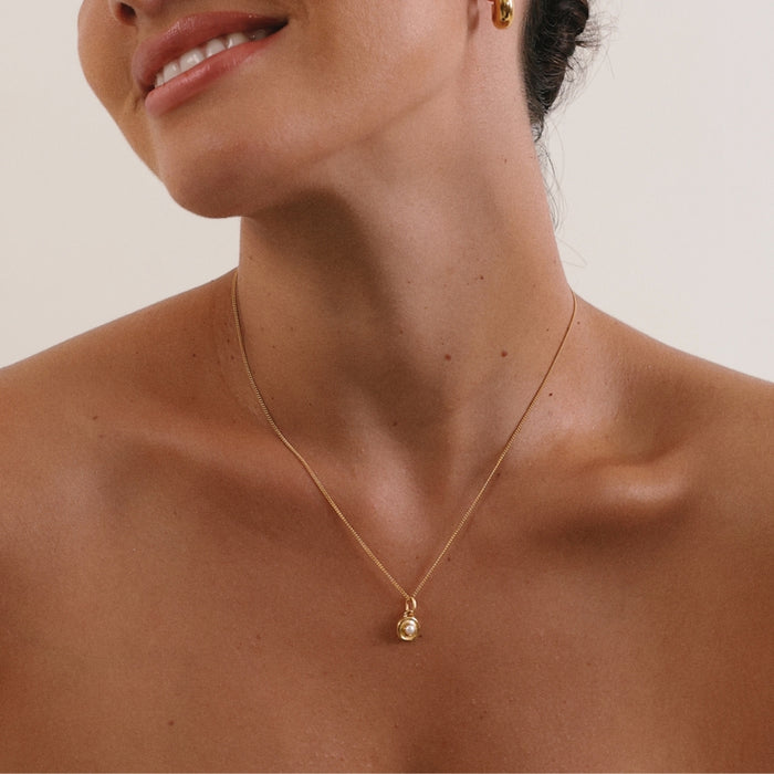 Close-up of a person wearing a gold necklace with a pendant on a neutral background