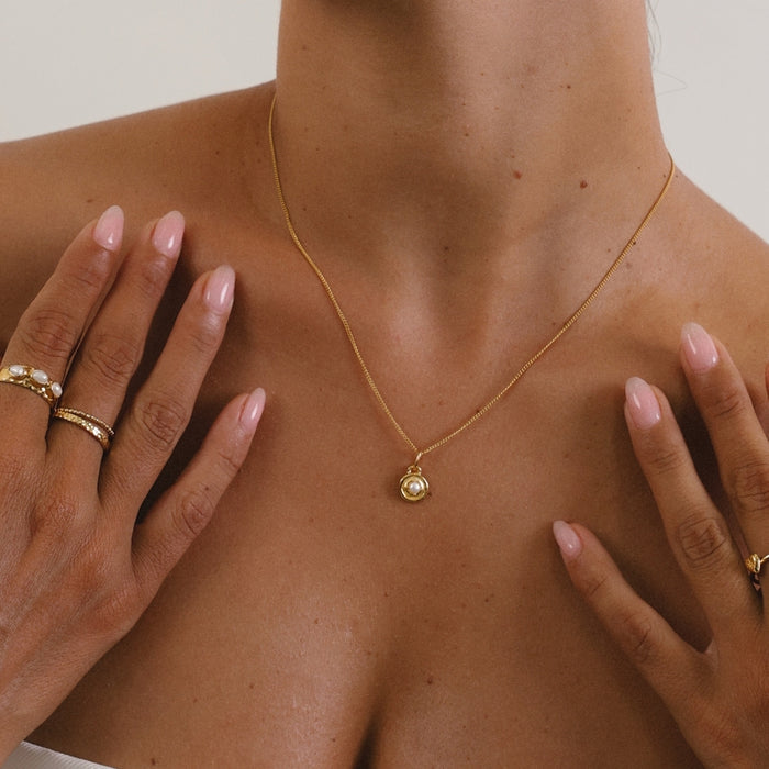 Gold necklace with a pendant on a person's neck, with hands gently touching the shoulders.