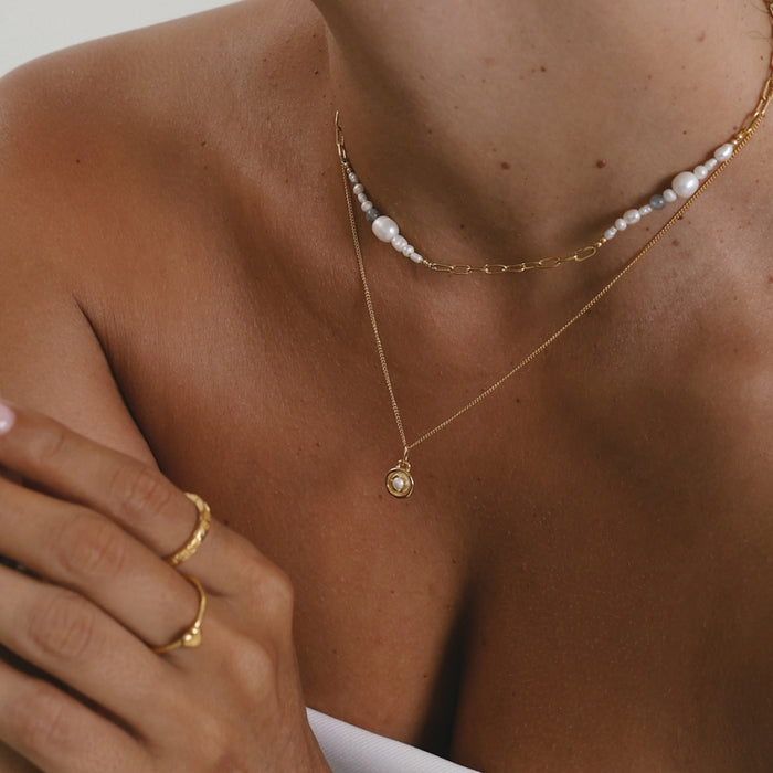 Close-up of a person wearing gold necklaces and a ring on a neutral background