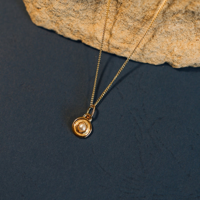 Gold necklace with a pendant on a dark surface