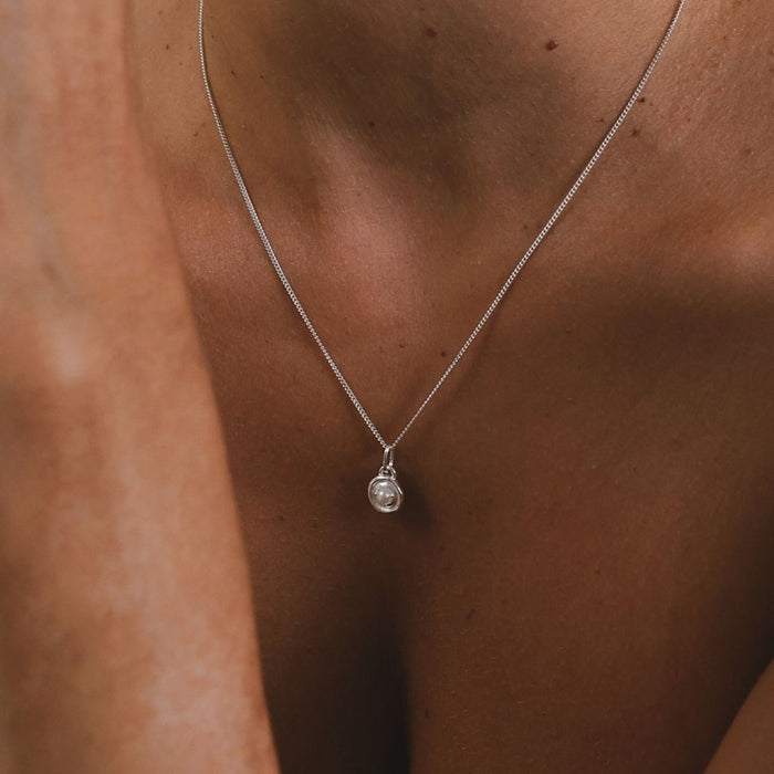 Silver necklace with a pendant on a person's neck against a brown background