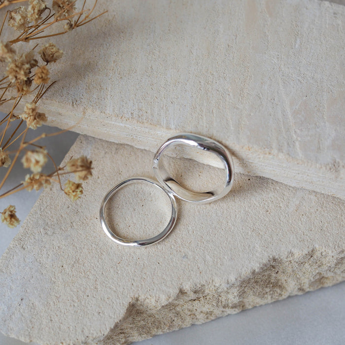 A pair of silver rings with organic, wavy designs displayed on beige stone