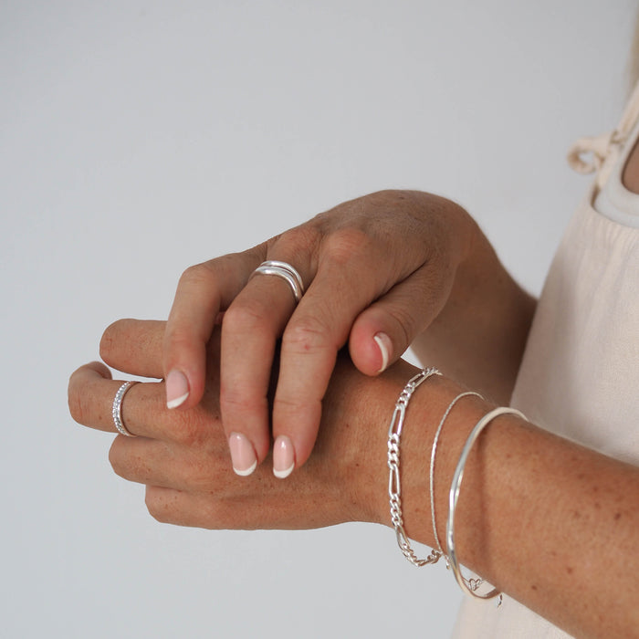 Close-up of a woman's arms  showcasing multiple silver rings and bracelets with various designs