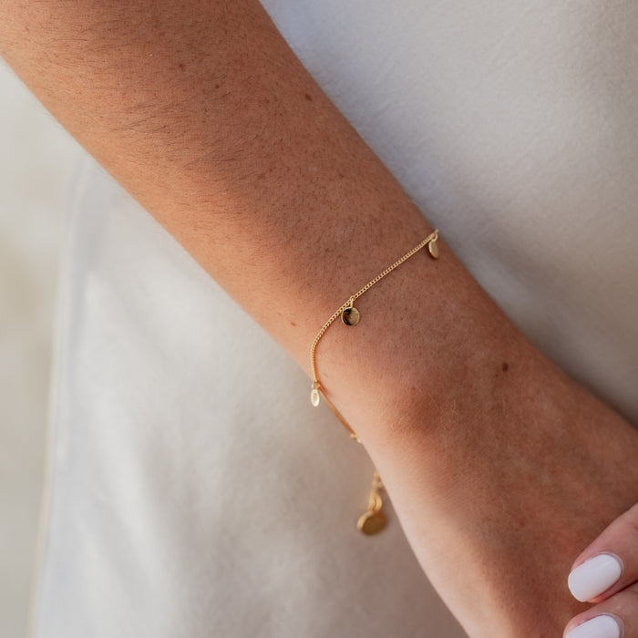 Close-up of a woman's wrist wearing a delicate gold bracelet with small circular charms.