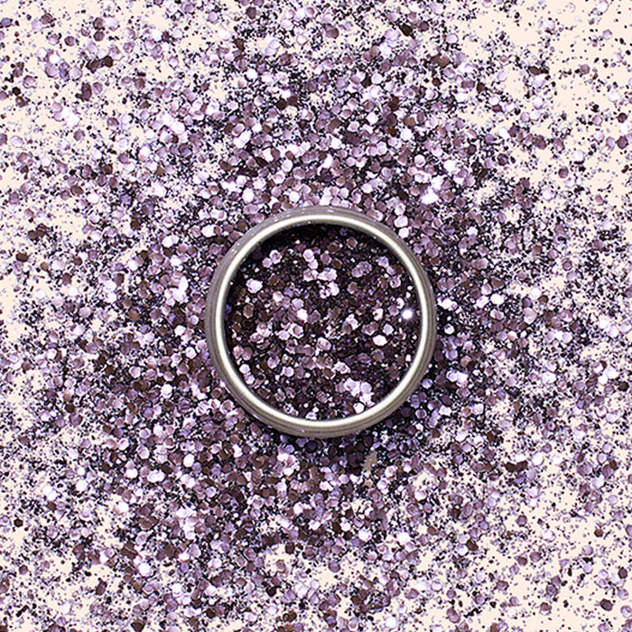 A silver ring sits on a surface dusted with Manucurist’s Lilac Biodegradable Glitter, creating a sparkling, colorful backdrop ideal for nail art inspiration.