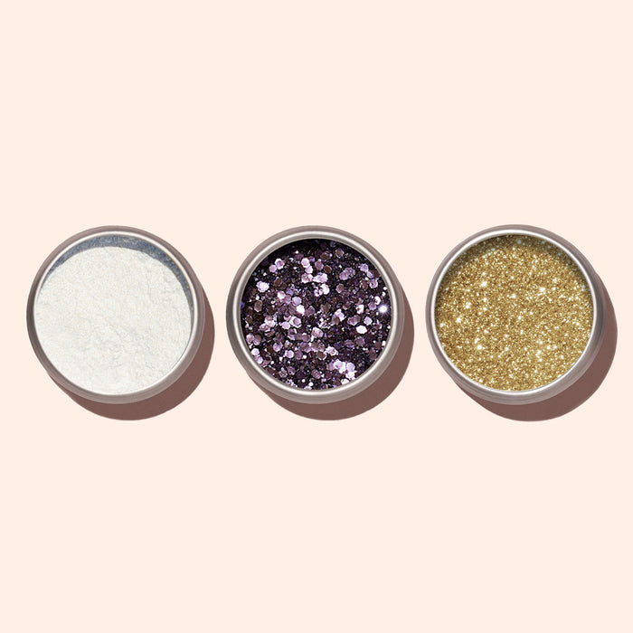 Three small round containers on a beige background feature Manucurist's Lilac Biodegradable Glitter in the center, surrounded by white fine glitter on the left and gold fine glitter on the right—ideal for sparkling nail art.