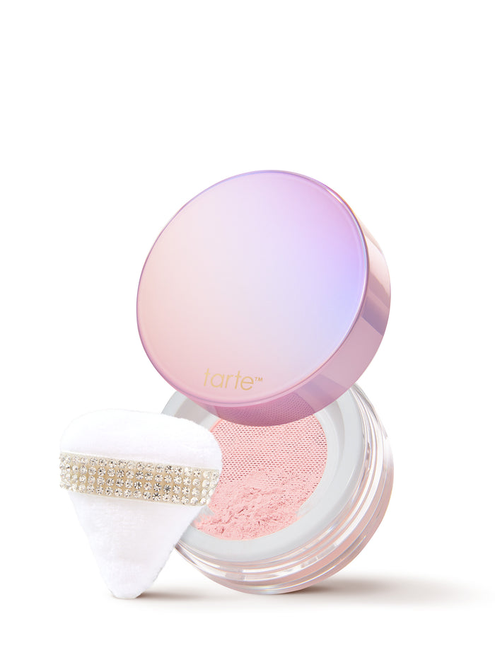 Tarte compact and striped gift box; compact lid open to show shimmering powder and fluffy white puff beside the box on a white background. Text: tarte
