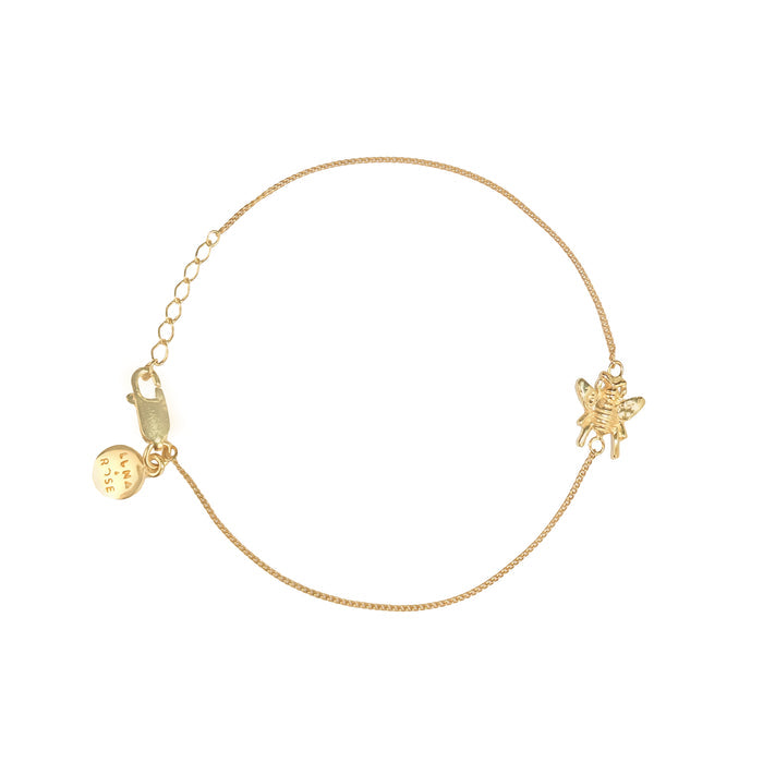 Gold bracelet with a small bee charm on a white background