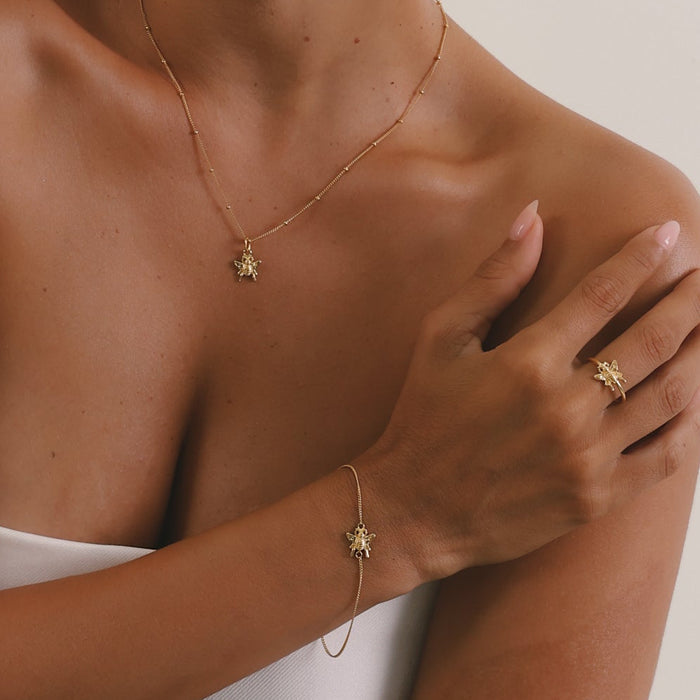 Woman wearing gold jewelry including a necklace, ring, and bracelet on a plain background