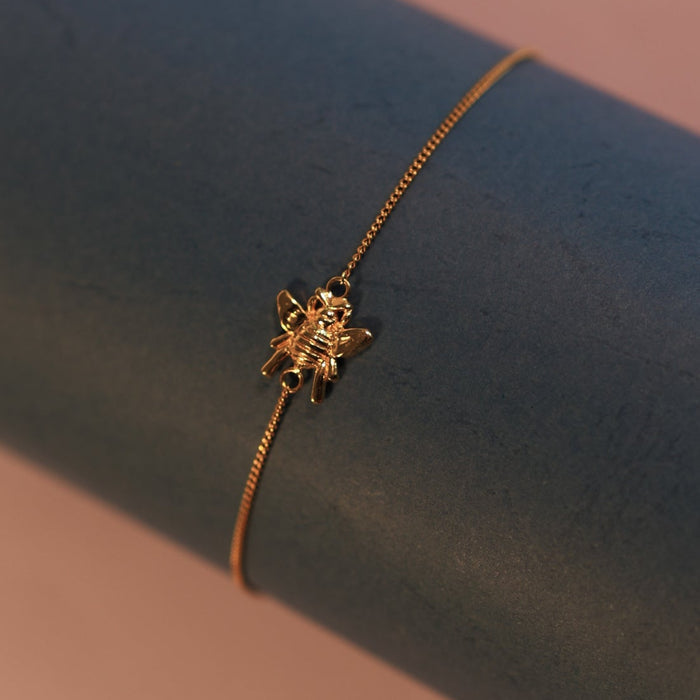 Gold bracelet on a dark blue surface with a soft pink background