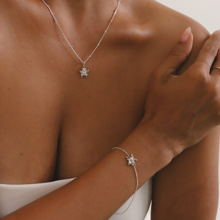 Person wearing a silver necklace and bracelet with a star-shaped pendant on a neutral background