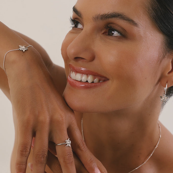 Woman wearing jewelry including a ring, bracelet, and earrings on a neutral background