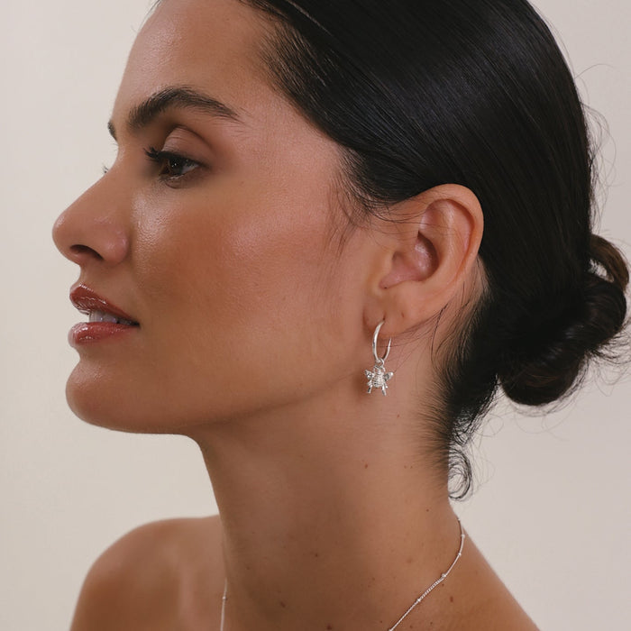 Woman wearing a silver necklace and earrings with a plain background