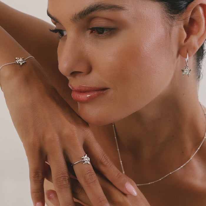 Woman wearing silver jewelry including a necklace, ring, and bracelet on a neutral background