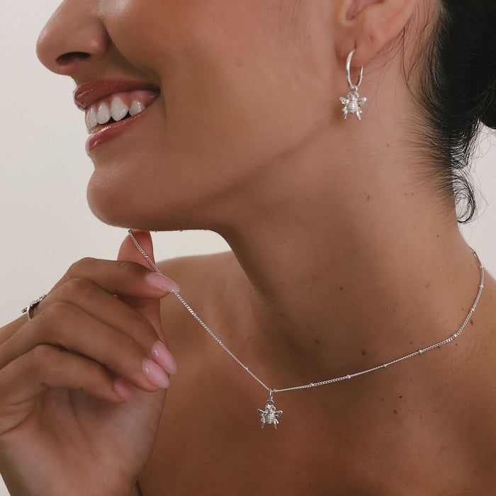 Woman wearing a silver necklace and earrings with a neutral background