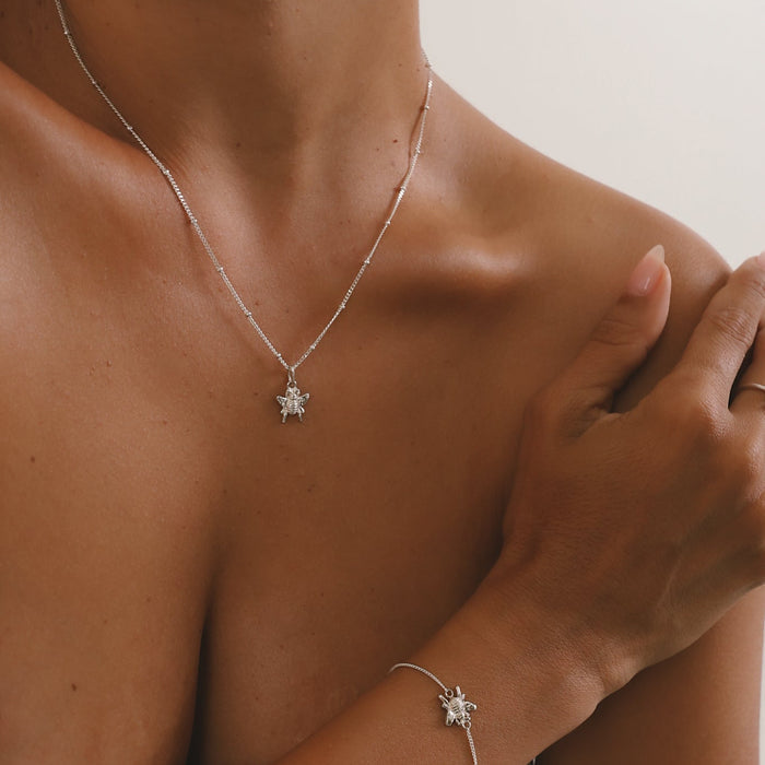 Person wearing a silver necklace and bracelet with a star-shaped pendant on a neutral background