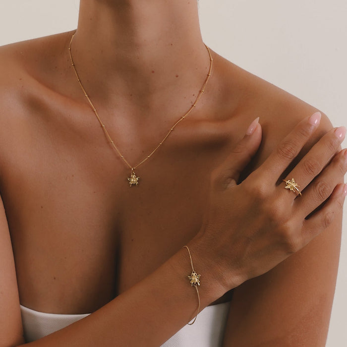 Woman wearing gold jewelry including a necklace, earrings, and bracelet on a neutral background