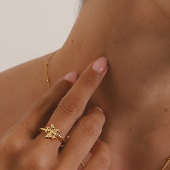 Close-up of a person wearing gold earrings and a ring with a neutral background