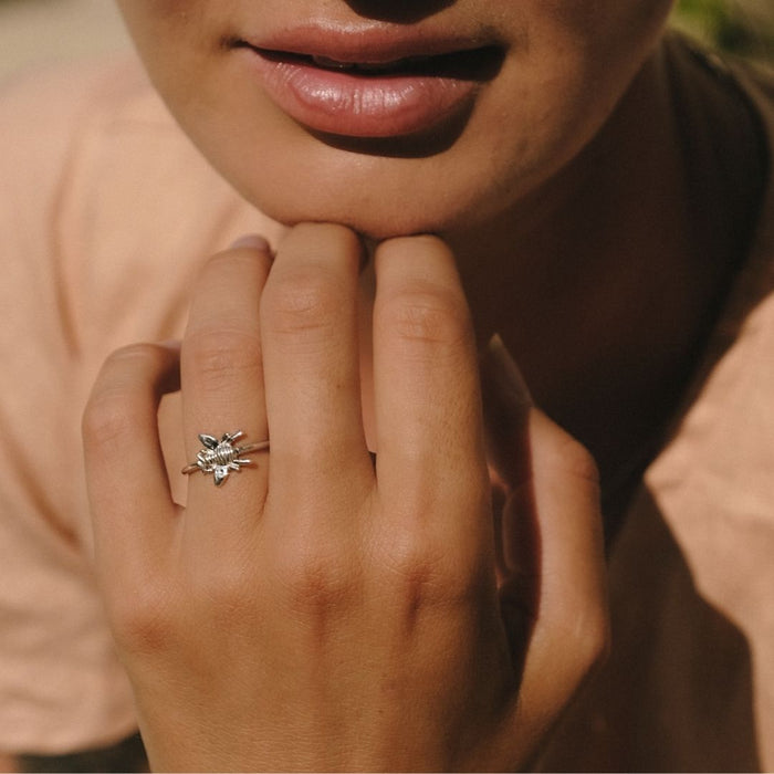 Close-up of a hand wearing a silver ring with a leaf design, against a blurred background.