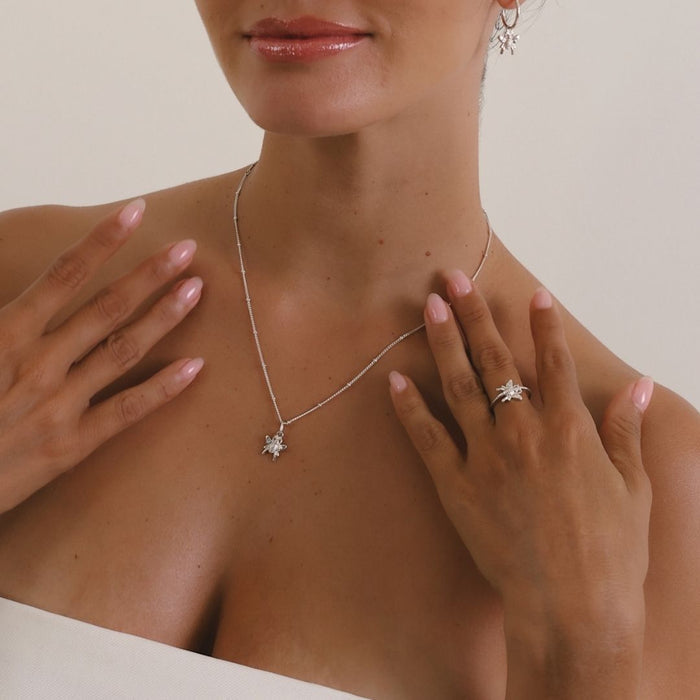 Woman wearing a silver necklace and ring with a neutral background