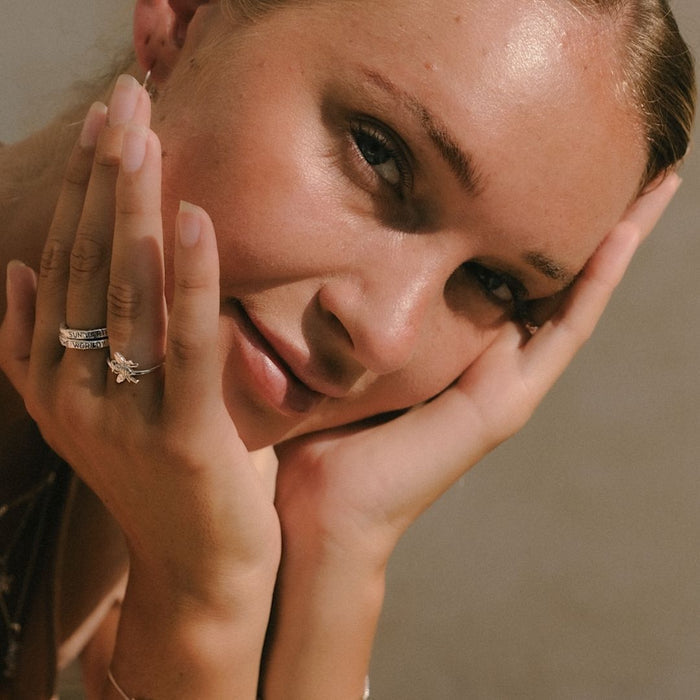 Close-up of a woman with her hands on her face, wearing rings.