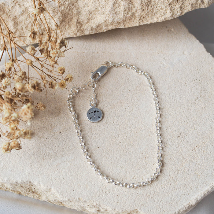 Close-up of a silver chain bracelet arranged on beige stone.