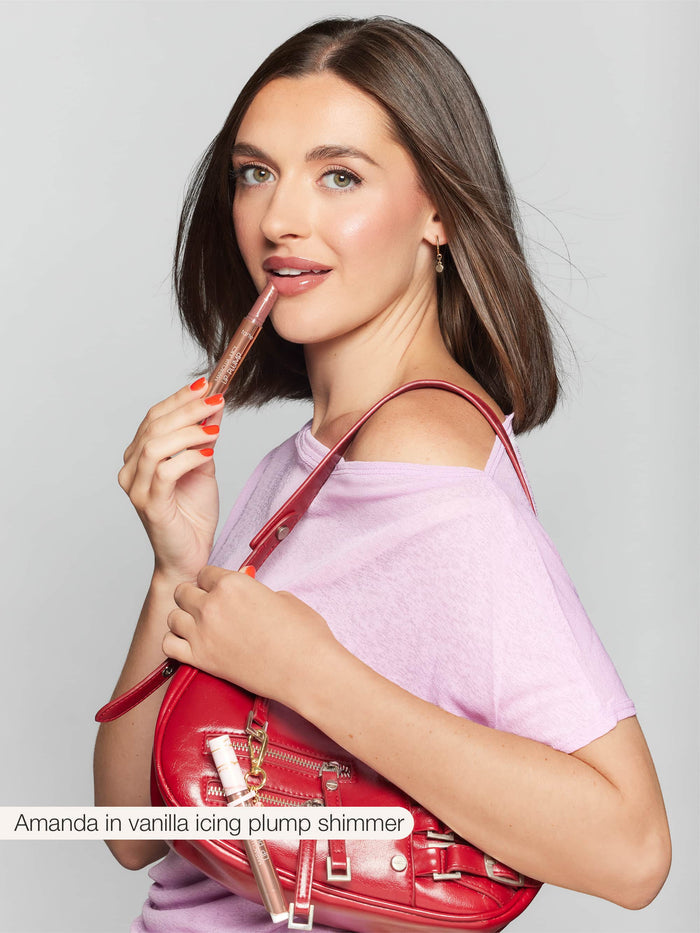 A person holds Tarte Cosmetics lip product near their lips, wearing a light purple top and carrying a red bag. Text reads: Amanda in vanilla icing plump shimmer.