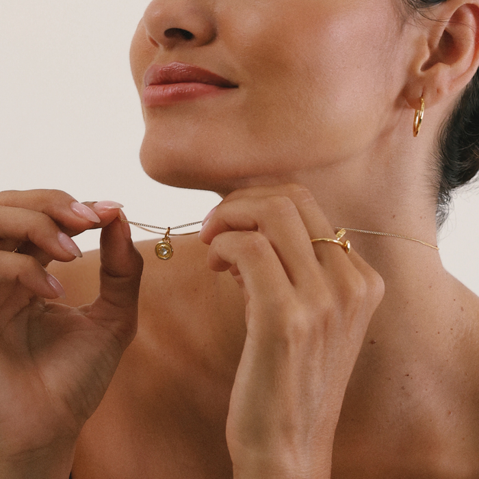 Woman adjusting a delicate gold necklace with a small pendant.