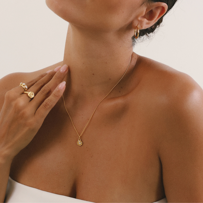 Woman wearing a gold necklace, ring, and earring on a neutral background