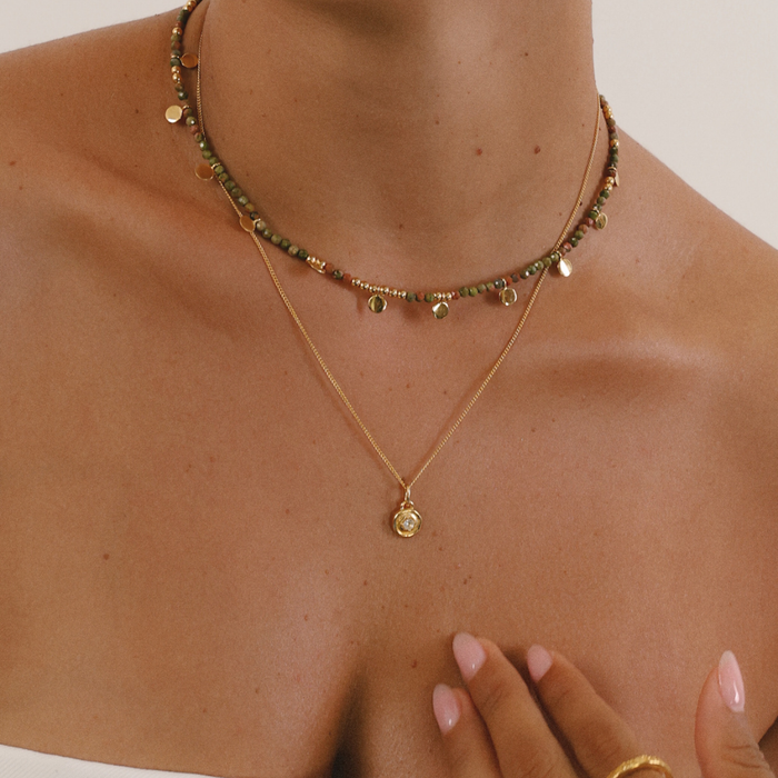 Two necklaces on a mannequin bust with a hand touching the skin.