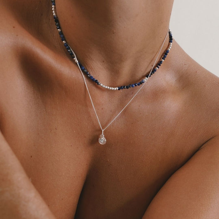Close-up of a person wearing two necklaces on a neutral background