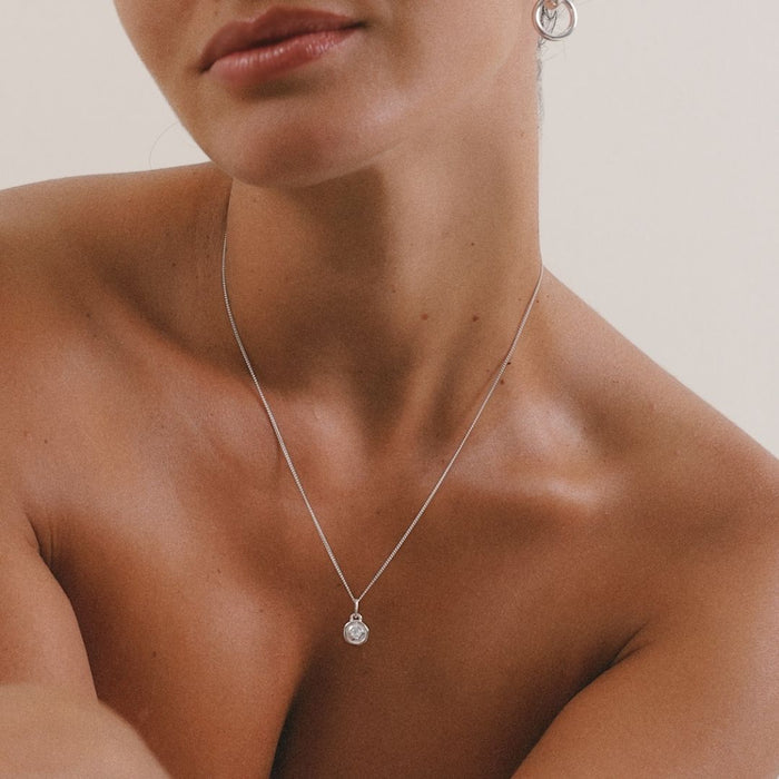 Close-up of a person wearing a silver necklace with a pendant on a neutral background