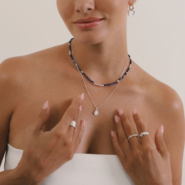Woman wearing a necklace and rings on a plain background