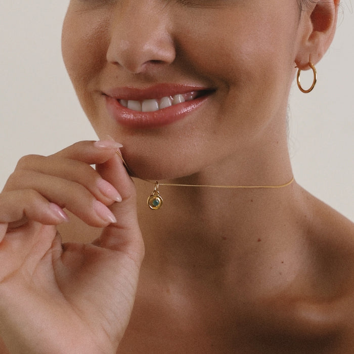 Woman wearing a gold necklace with a pendant, close-up on face and neck.