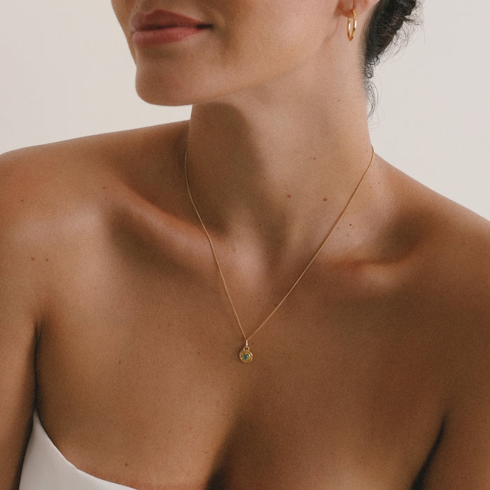 Close-up of a person wearing a gold necklace with a small pendant.