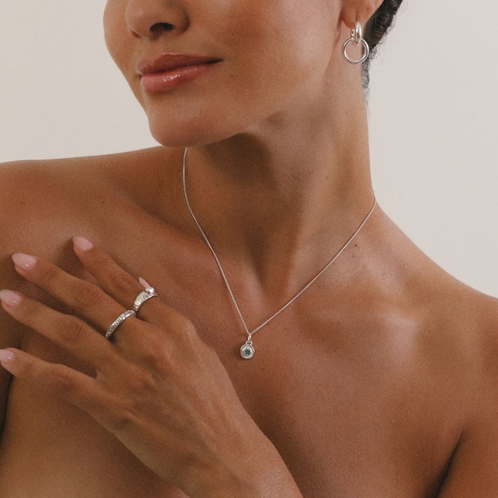 Woman wearing a silver necklace, ring, and earrings on a neutral background