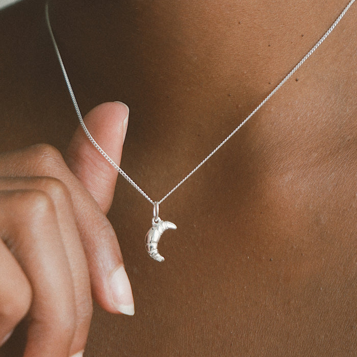 Mini Croissant Necklace in Silver from the ACME x Luna & Rose collection, a delicate croissant-shaped pendant perfect for layering or wearing solo.