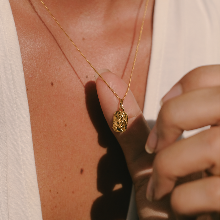 Close-up of a person wearing a gold necklace with a pendant.