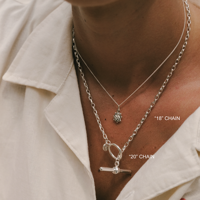 Silver chain necklaces with pendant on a person wearing a white shirt.