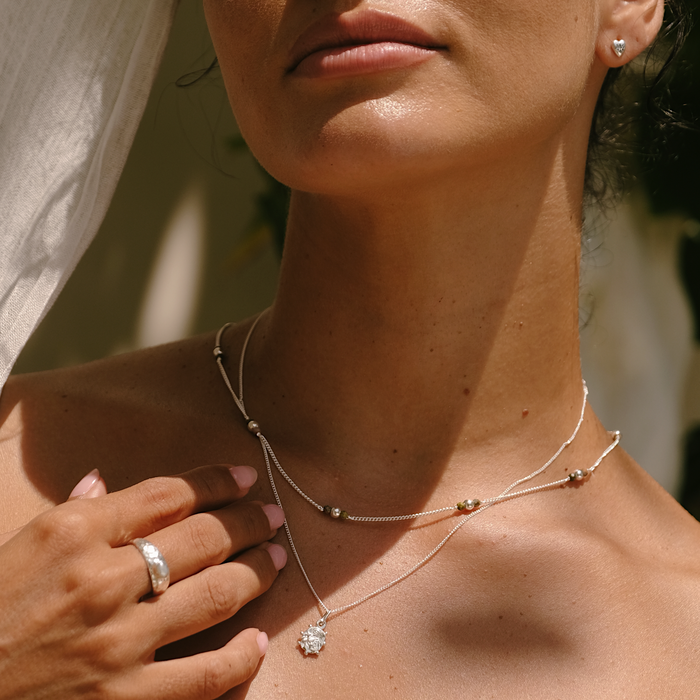 Close-up of a woman wearing a delicate necklace with a diamond pendant, with a blurred natural background.