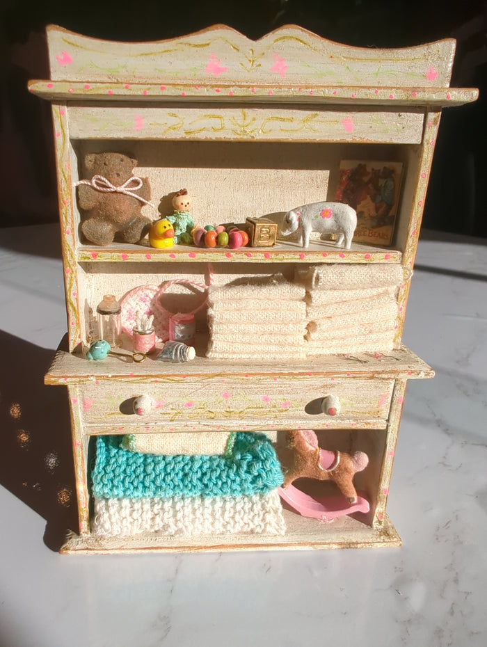 Detailed miniature nursery hutch scene by Detail In Miniature, showcasing tiny furniture and accessories in a charming display.